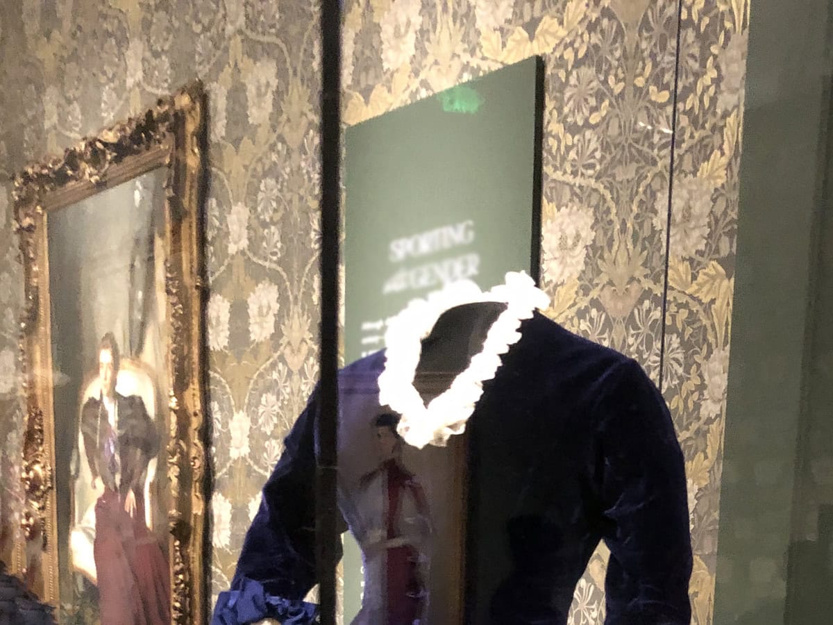 A dress and painting on display in a museum gallery with brocade walls