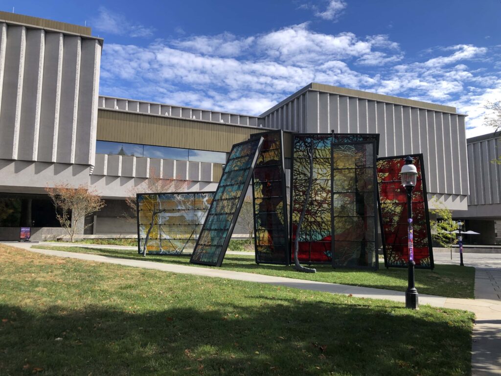 A grey modernist building with a modern stained glass installation in front.