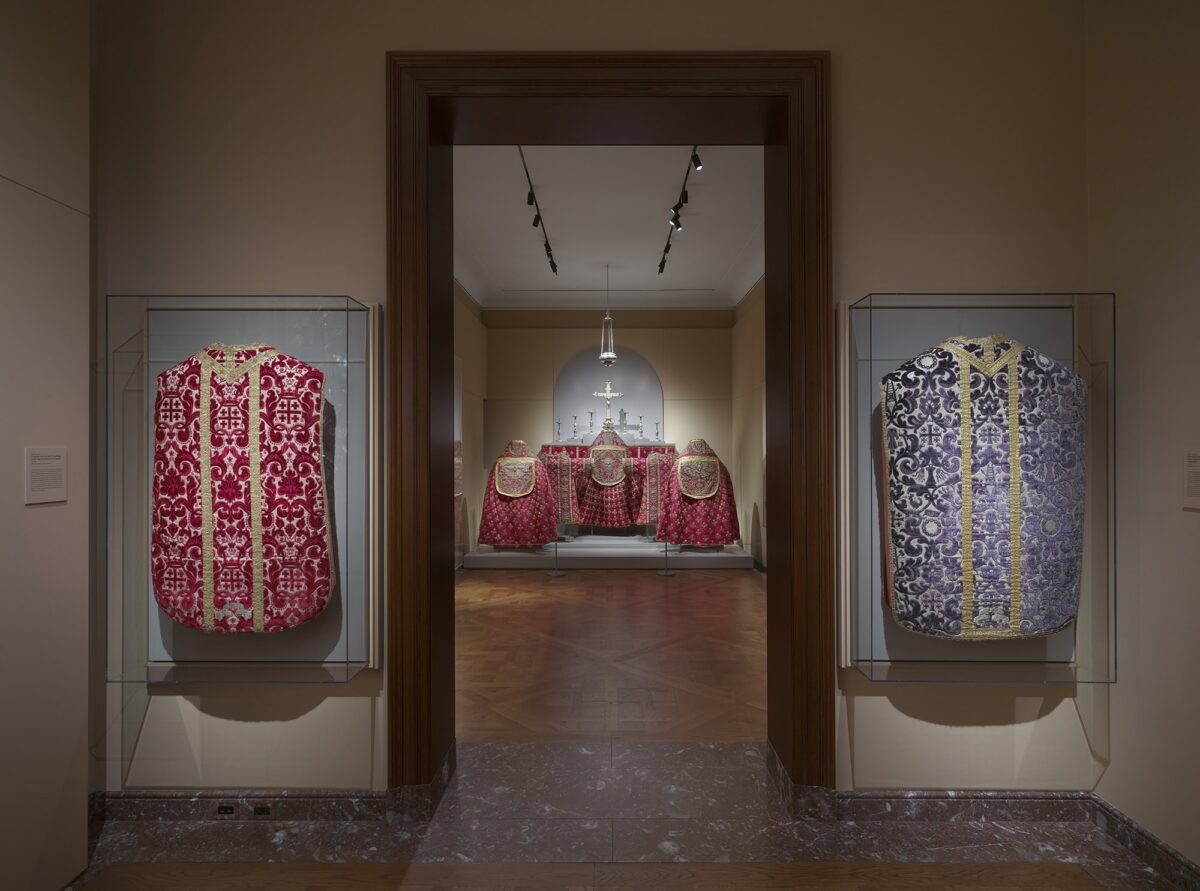 One room looking into another, both with red and blue embroidered church vestments