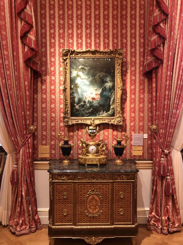 A painting above an ornate table in a room with red walls and curtains