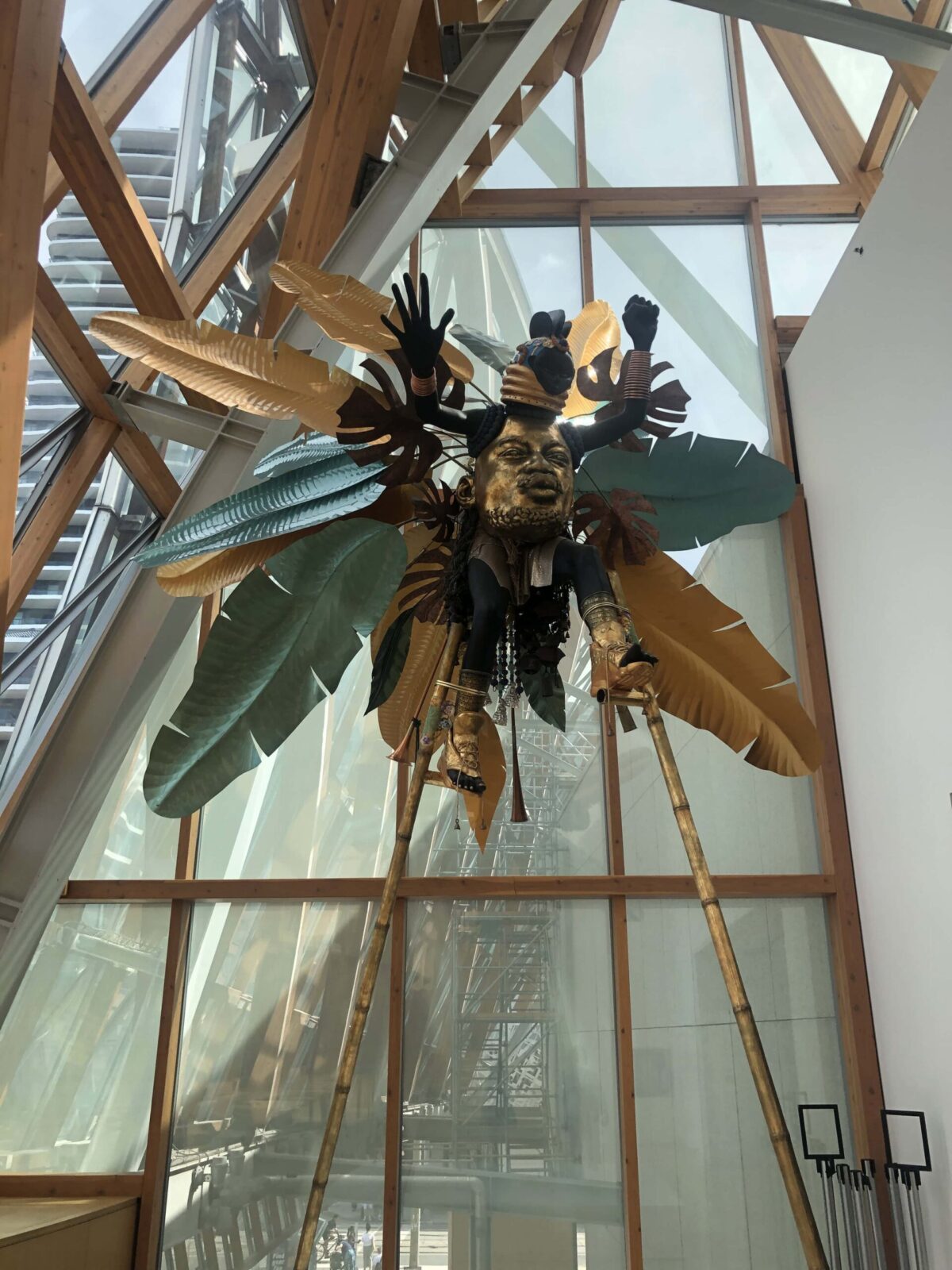 A large, multi-media sculpture depicting a man on stilts in a costume with feathers